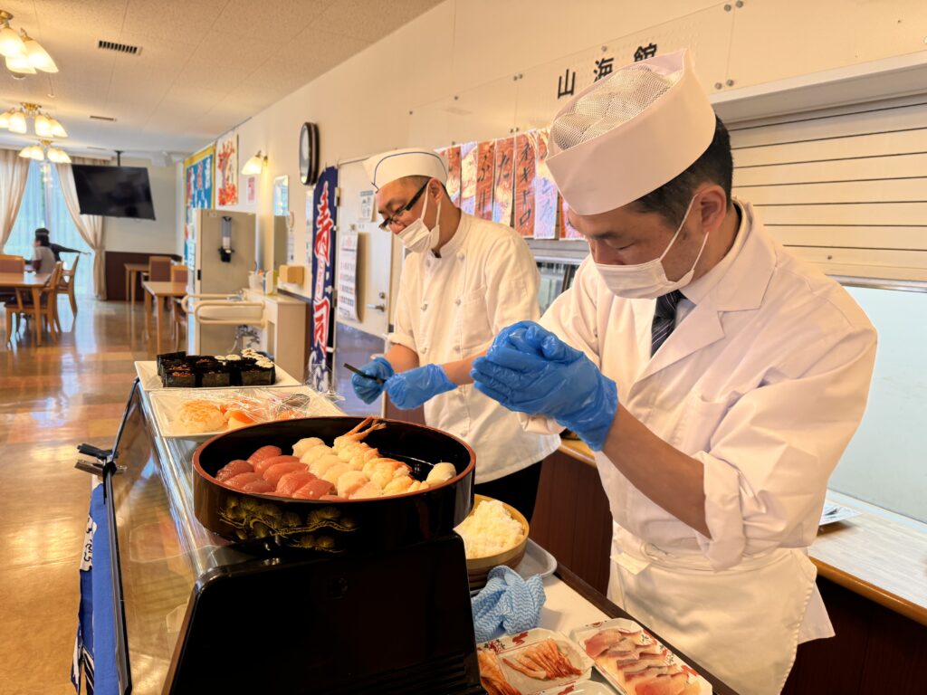 介護施設のキッチンで職員が調理実演・食事準備を行っている風景